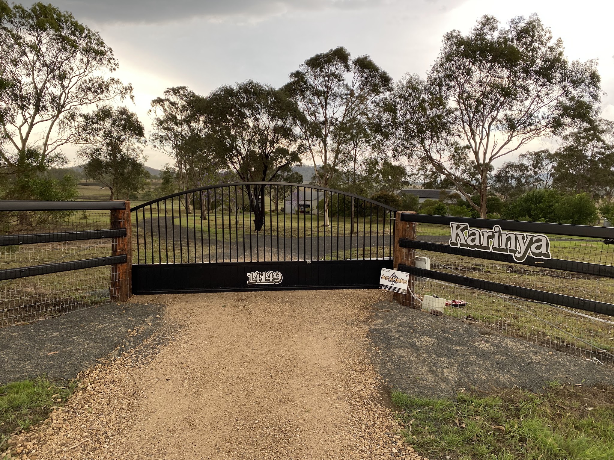 Wide view of the arched steel sliding gate between timber posts and black rail fencing